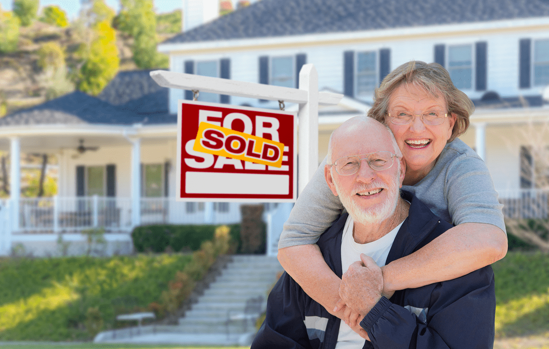 Smiling pair with sold house sign